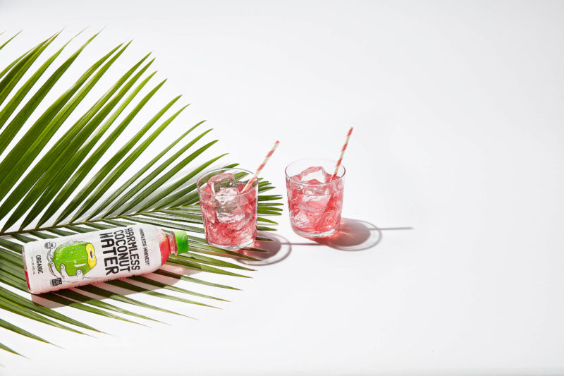 Two glasses of Harmless Coconut Water in iced glasses, with a palm leaf